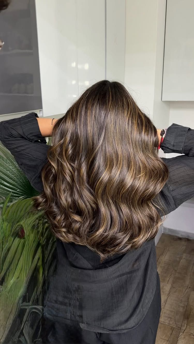 Wavy brown hair with subtle warm caramel balayage highlights in a salon