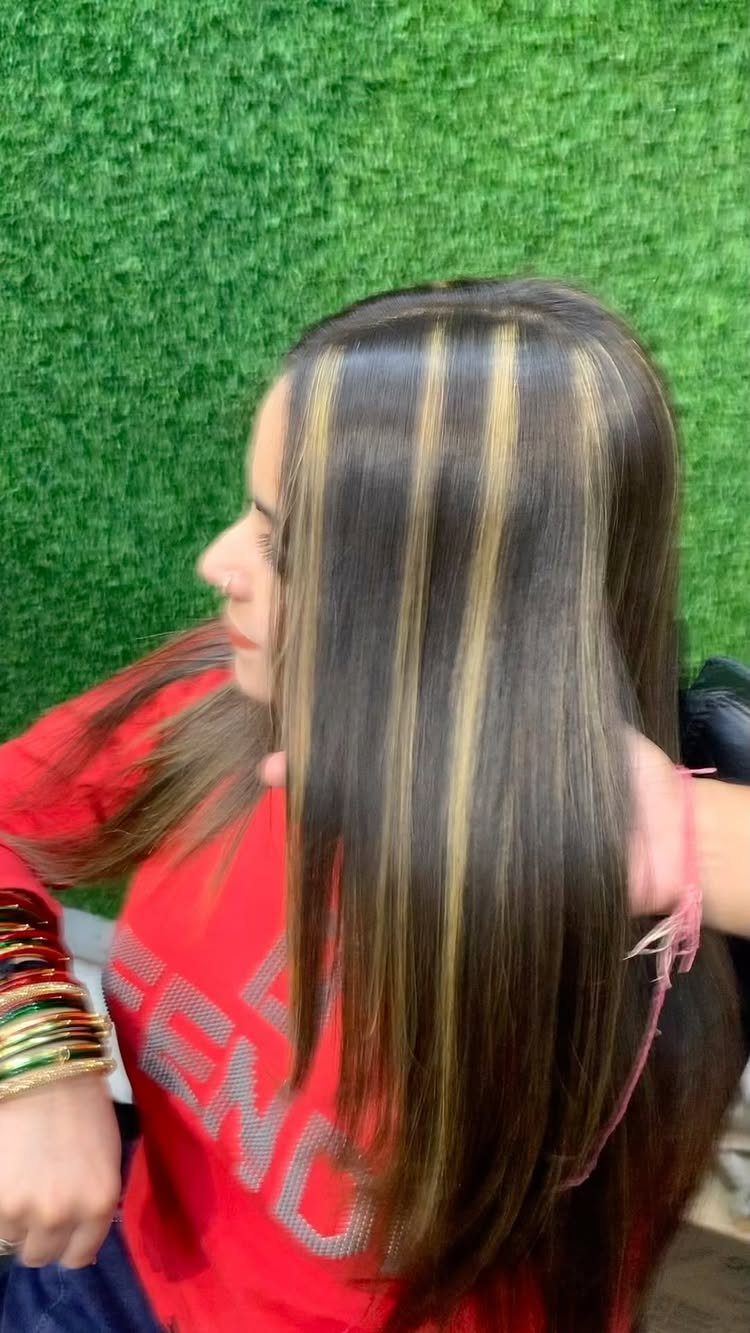 Long dark brown hair with broad golden blonde highlights against a green wall