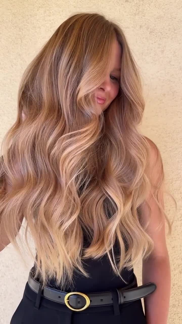 Woman showcasing long, wavy golden blonde hair with warm honey and bronze tones