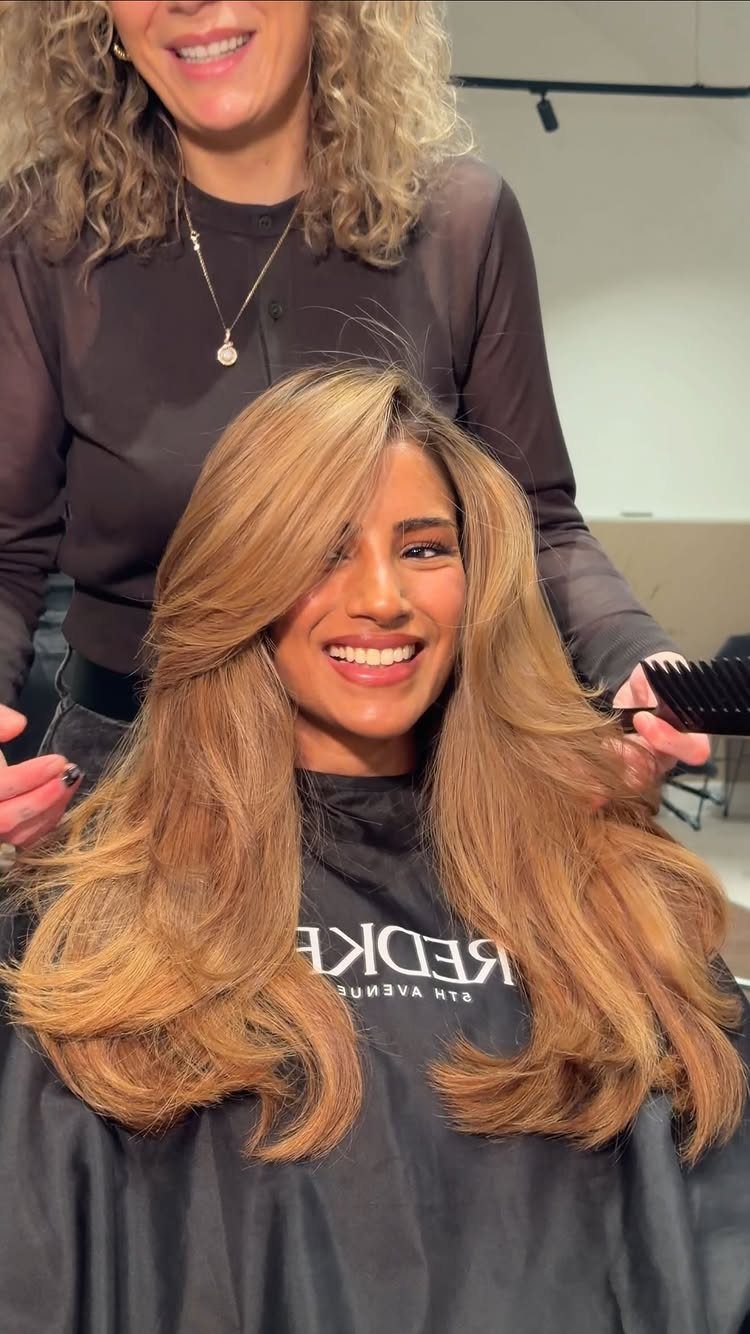 Woman displaying long honey-blonde highlighted hair with softly curled ends