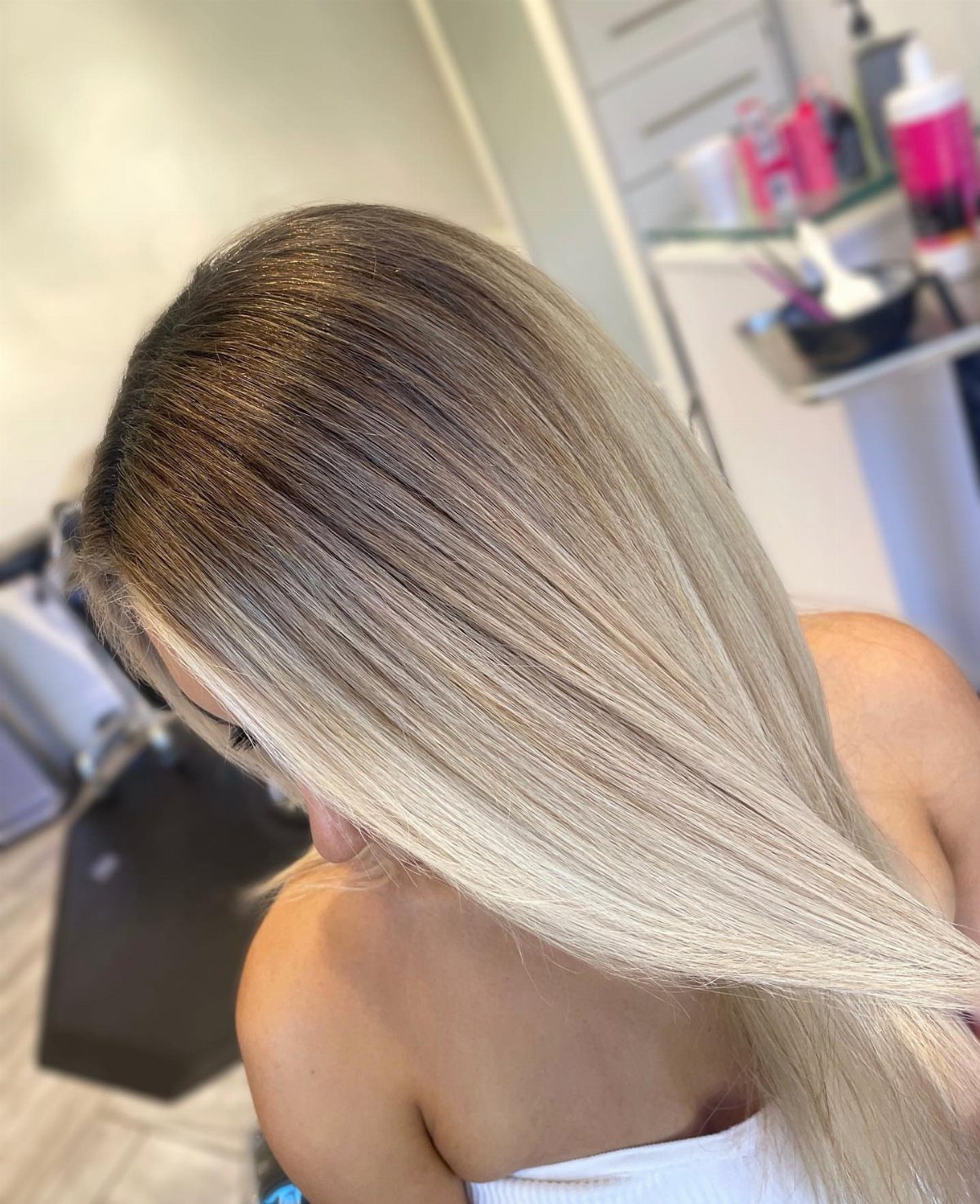 Long blonde hair transitions from dark roots through warm beige to icy silver ends.