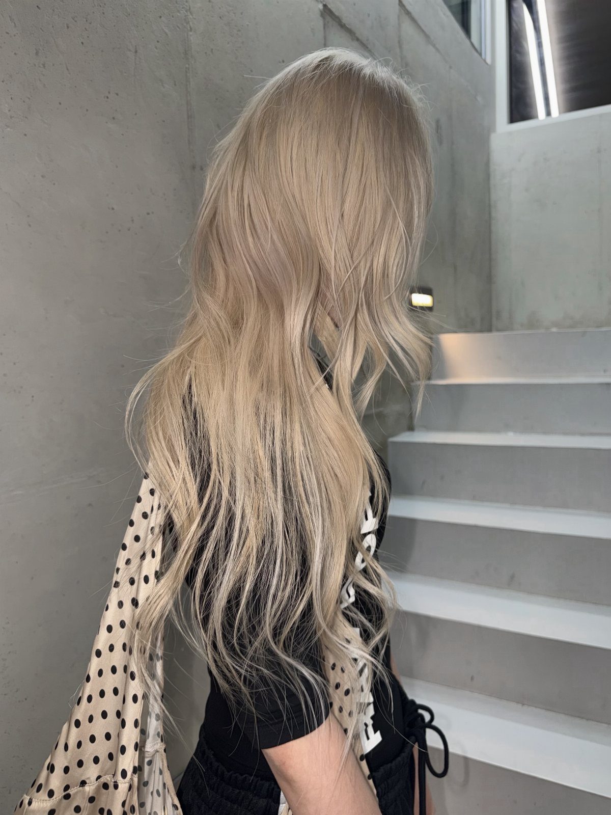 Long pale ash-blonde hair with darker ends falls over a black top