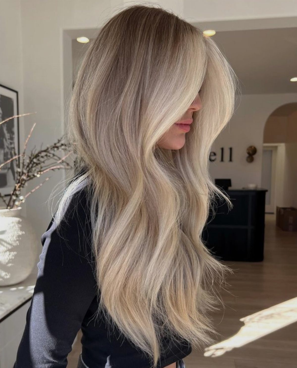 Long ash-blonde hair with lighter face-framing sections over a dark top