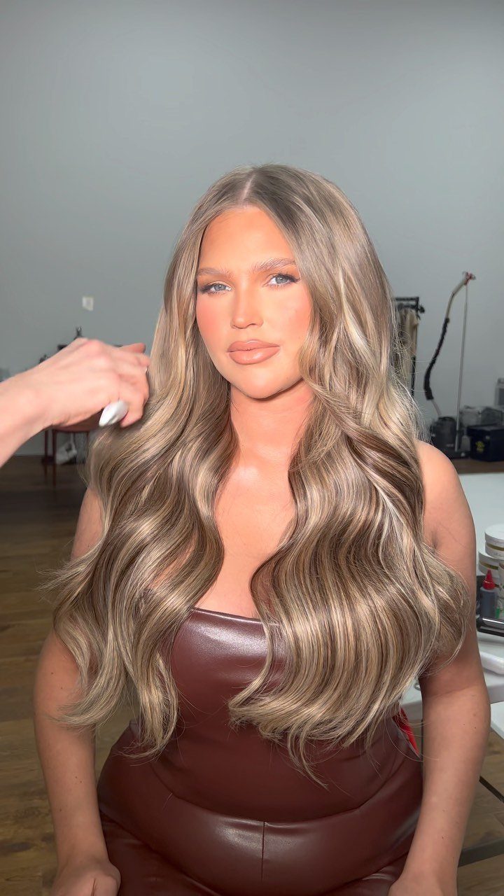 Woman with long ash-blonde waves showing darker natural roots in a salon