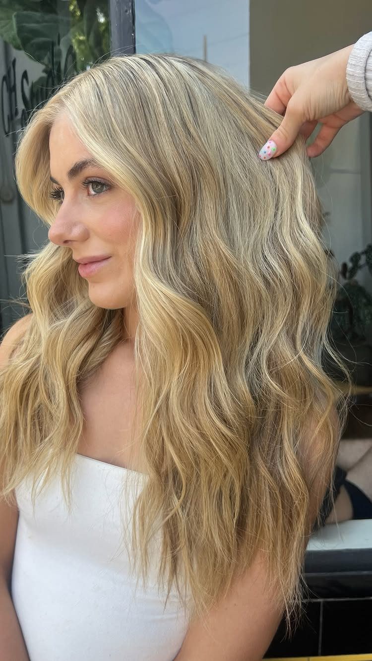 Long, softly waved sandy blonde hair with darker roots in a salon