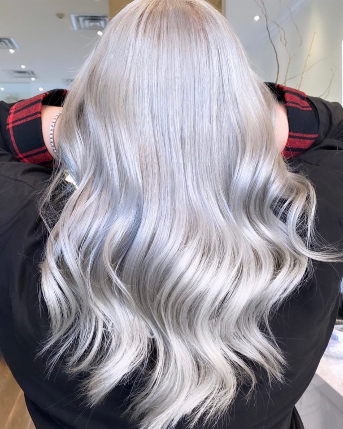 Long silver-blonde waves with cool gray streaks shown from behind in a salon