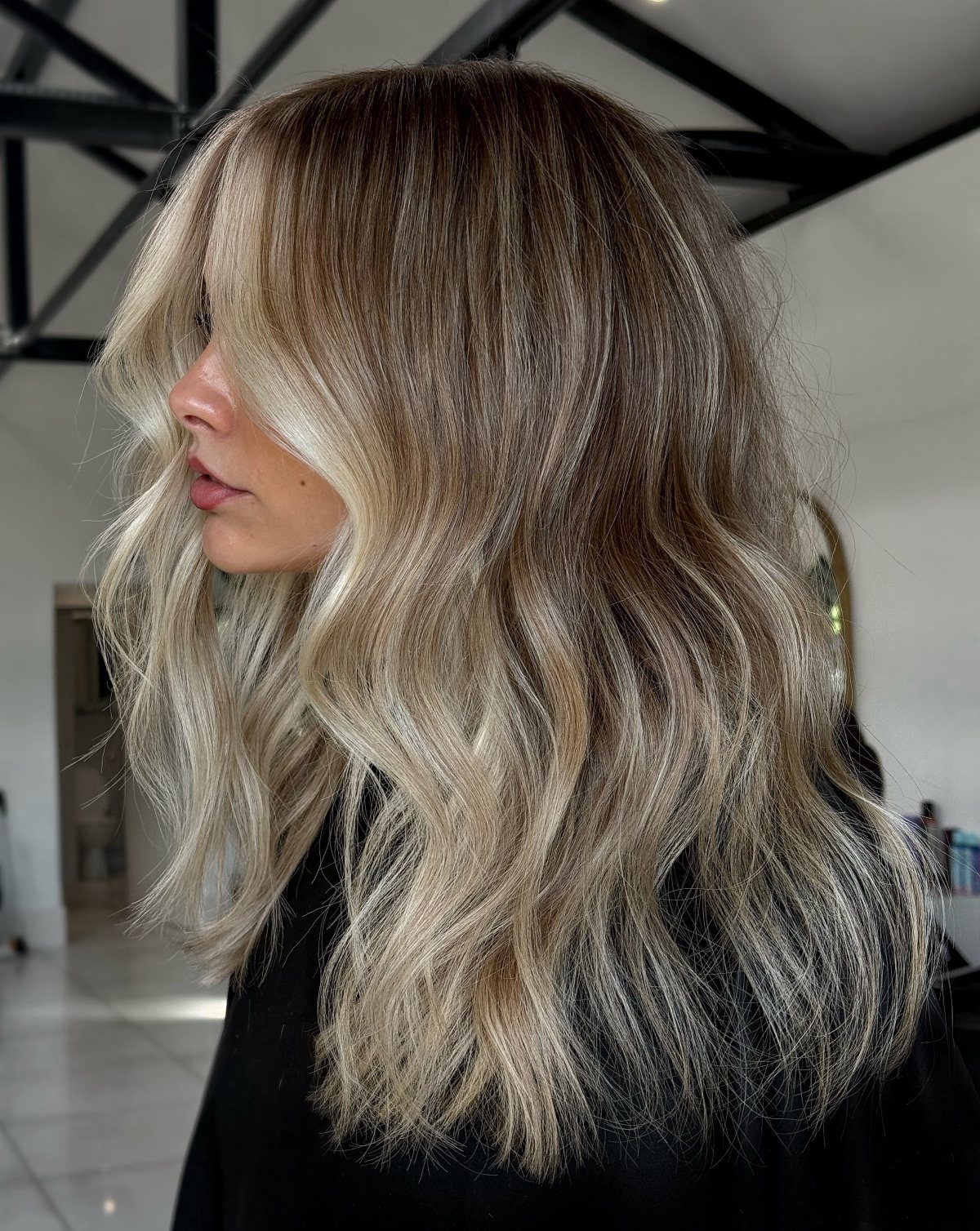 Woman with long wavy blonde hair, dark roots, and lighter face-framing strands