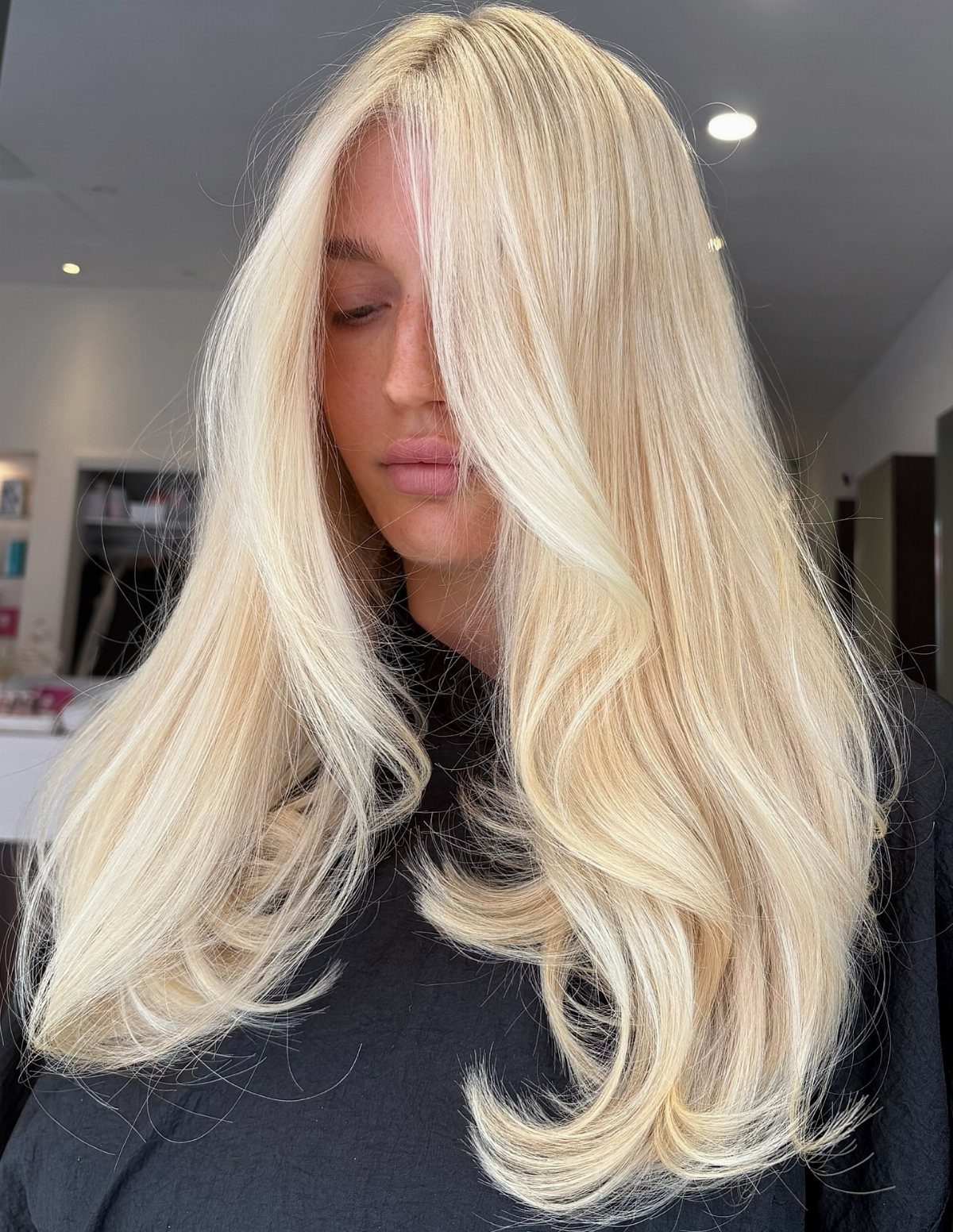 Long wavy buttery blonde hair styled over a dark salon cape