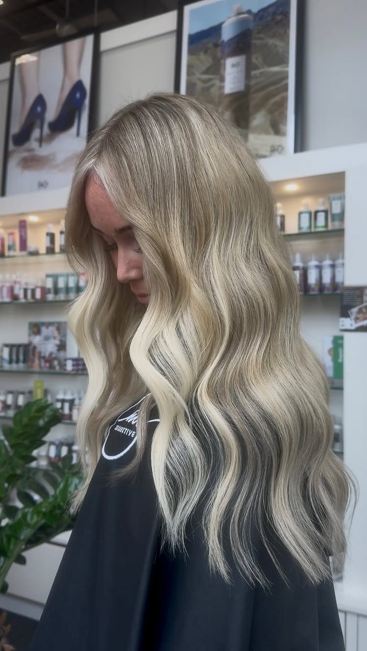 Woman with long wavy blonde hair showing creamy highlights and darker roots