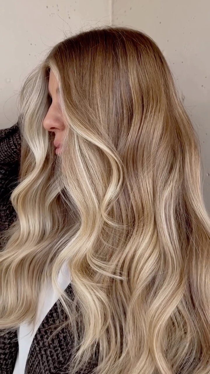 Long creamy blonde waves with darker roots frame a woman's profile.