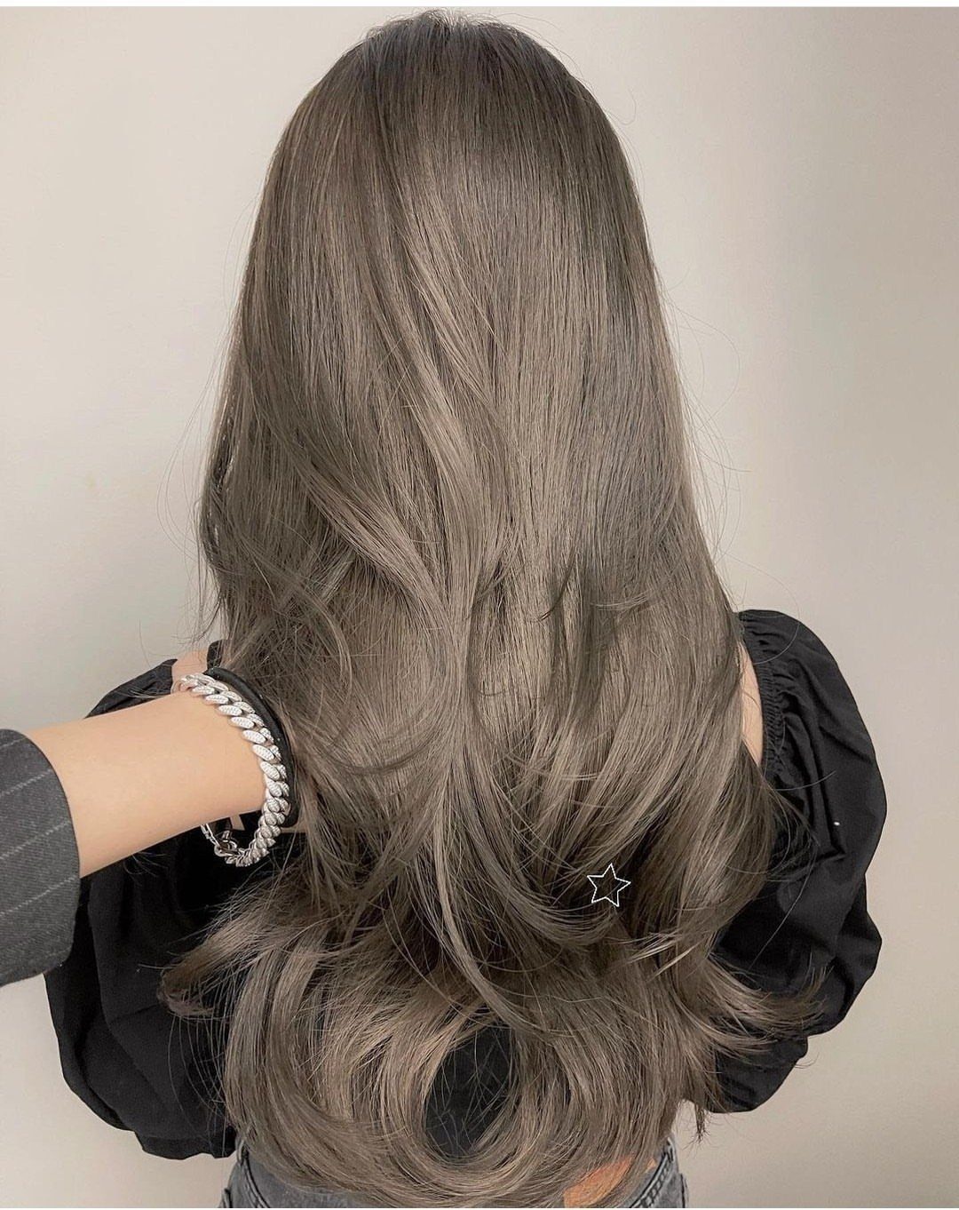 Long, cool dark ash blonde hair falls in layered curls against a beige wall.