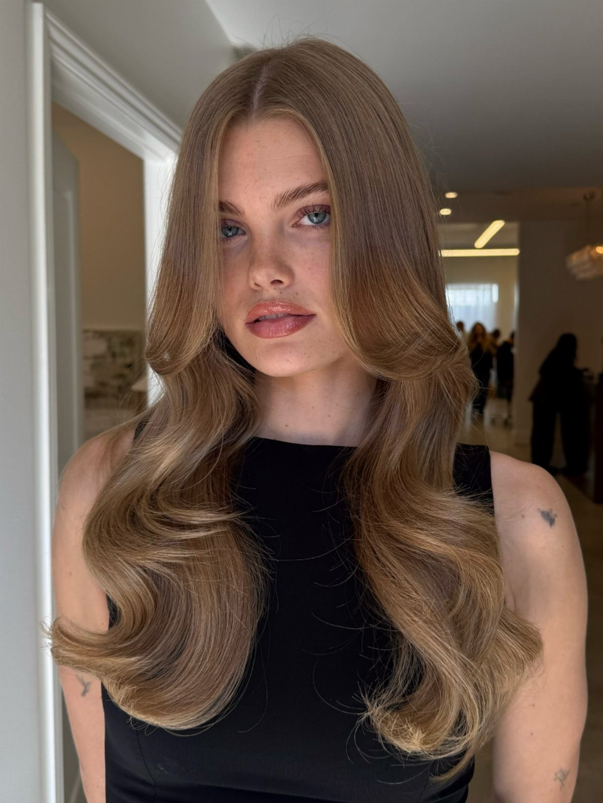 Woman with long, curled dark blonde hair wearing a sleeveless black top