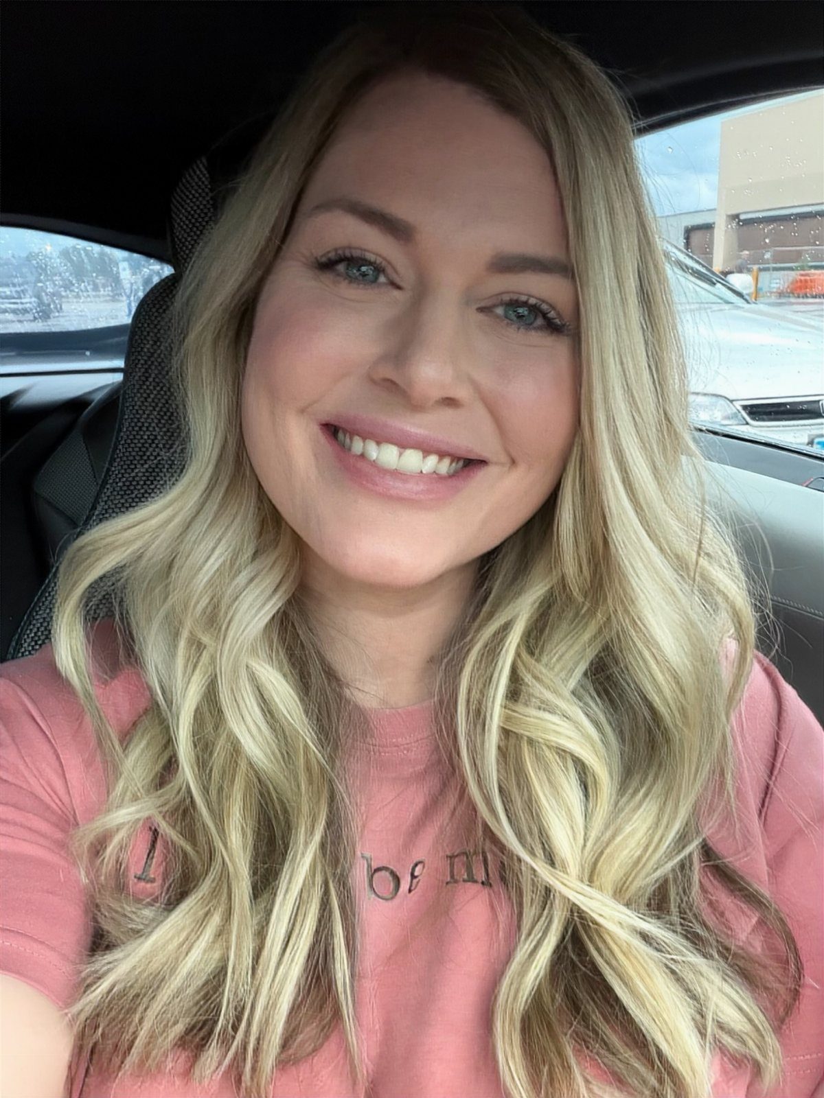 Woman with long, wavy blonde hair and darker roots sitting in a car