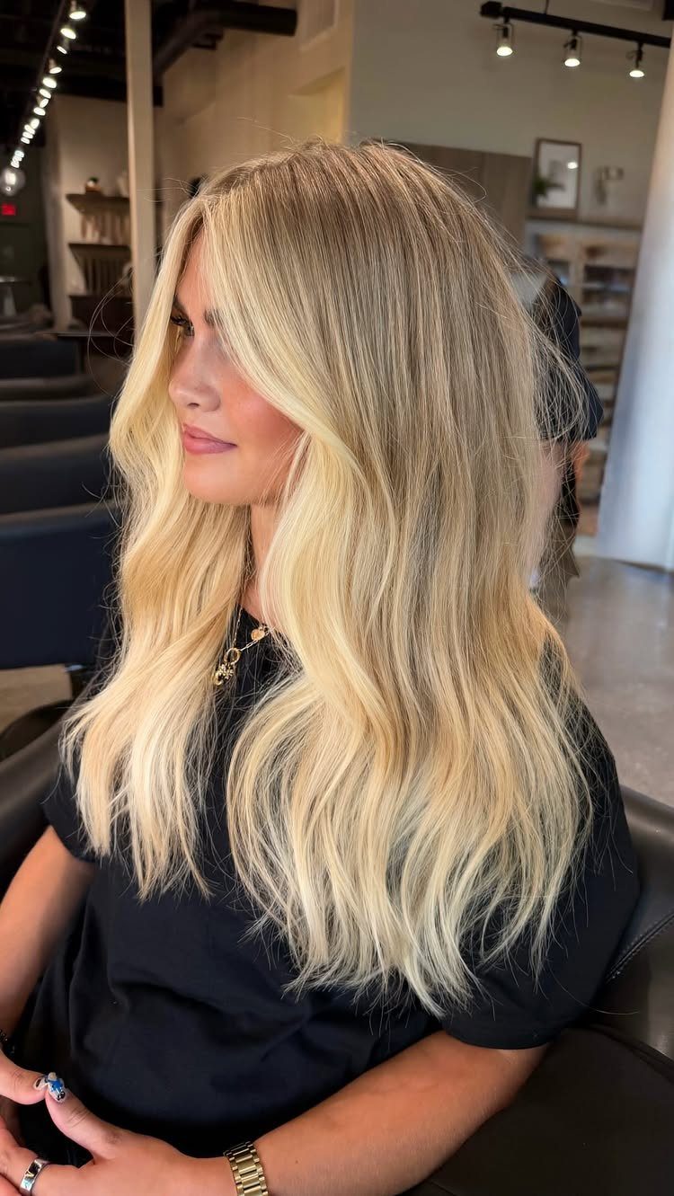 Long blonde hair with darker roots falls in soft waves over a seated woman's shoulders.