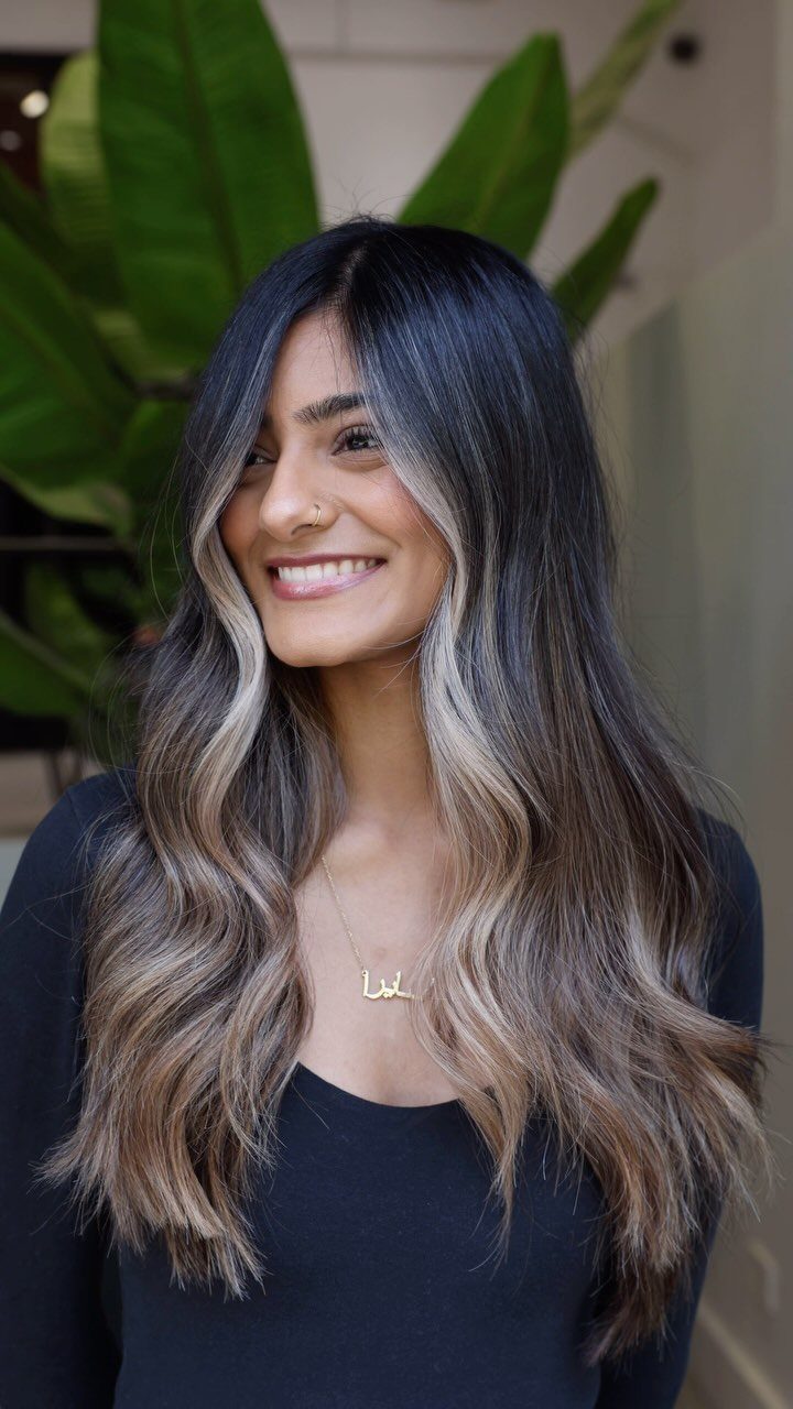 Woman with long dark hair and cool ash-blonde highlights smiling indoors