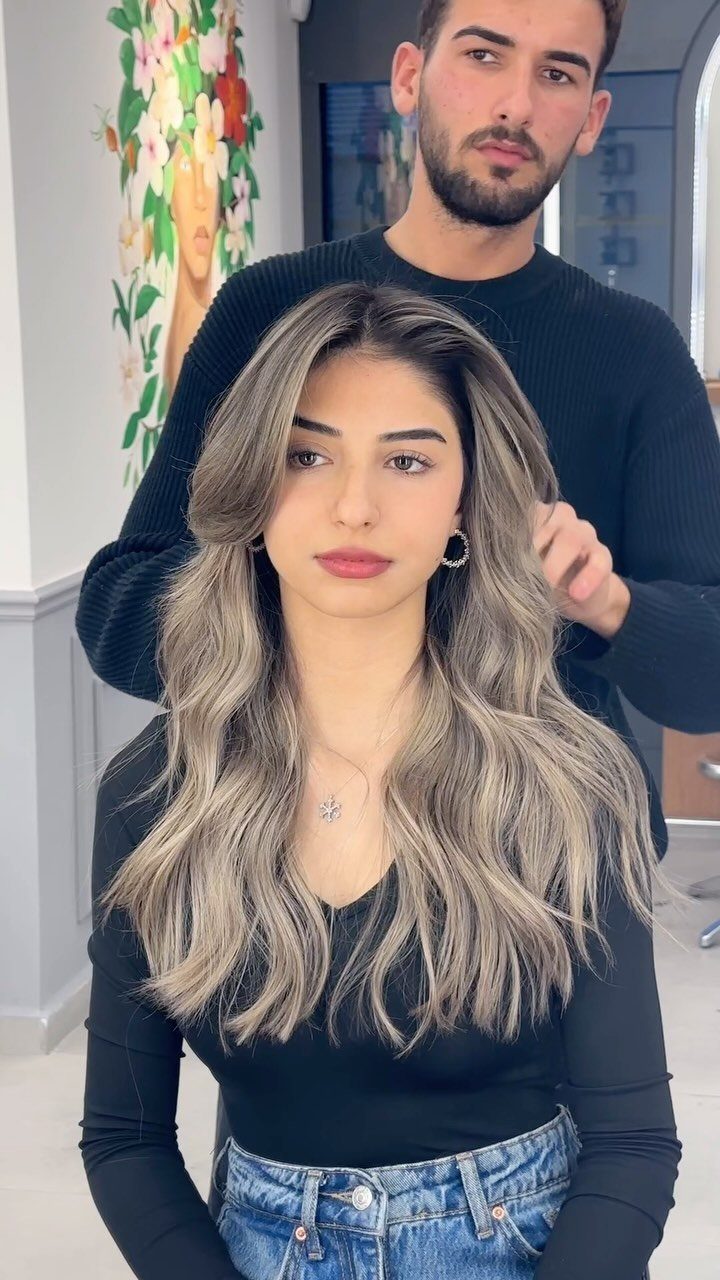 Woman displaying long, wavy beige-blonde hair with a stylist standing behind her