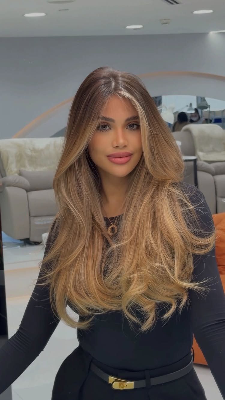Woman displaying long wavy caramel balayage hair with darker roots