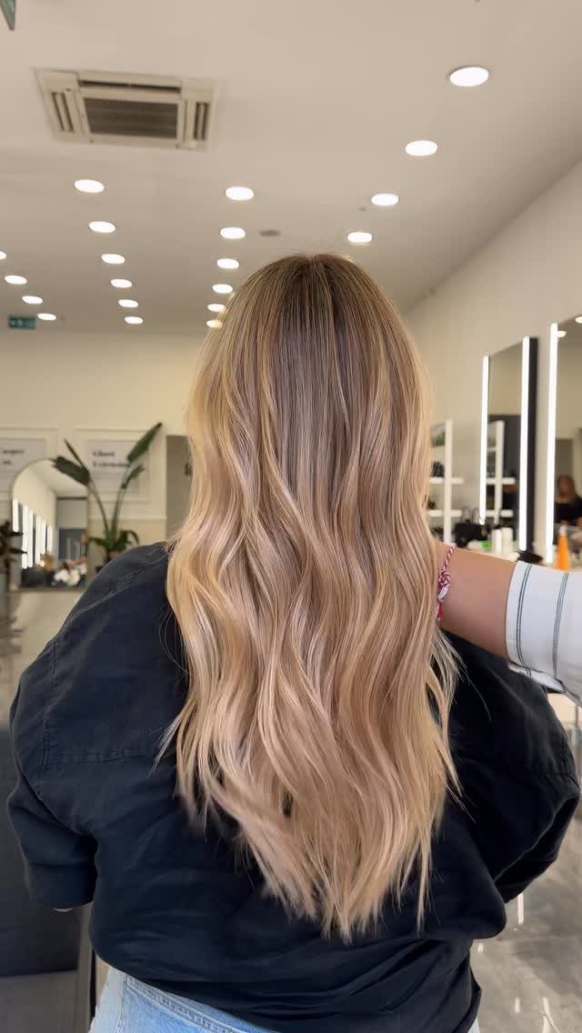 Long wavy blonde hair with darker roots styled down the back in a salon