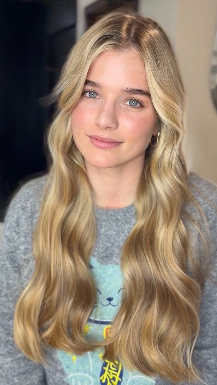 Woman with long, wavy golden blonde hair and a center part