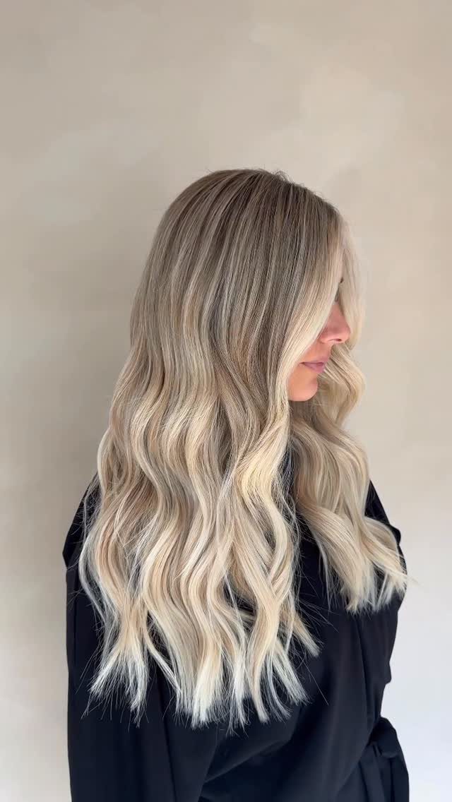 Long wavy hair blends dark roots into pale icy blonde balayage.