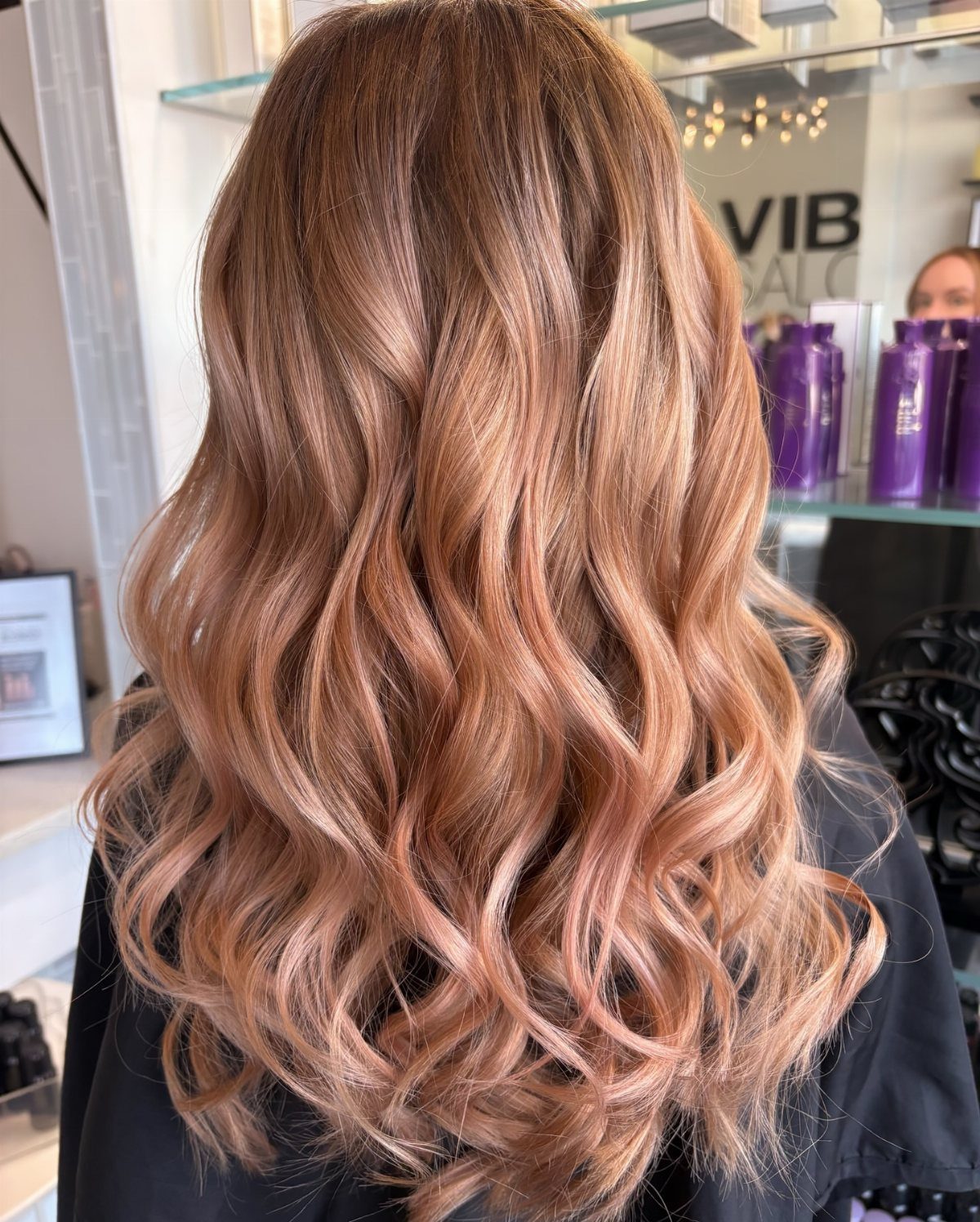 Long rose-gold blonde waves shown from behind in a salon