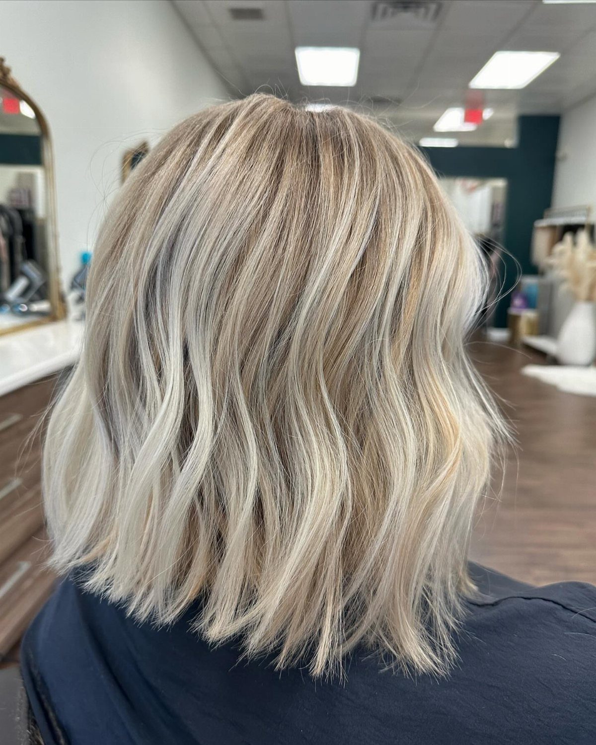 Short blonde bob with pale balayage highlights and darker roots in a salon