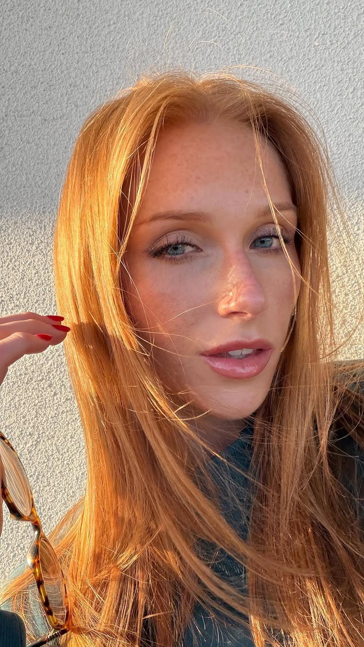 Woman with long warm strawberry blonde hair posing in sunlight