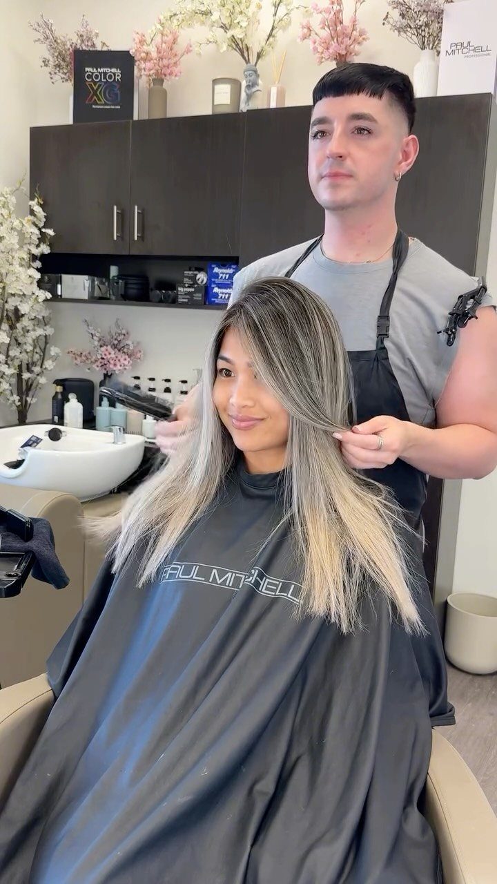Woman displaying long ash blonde balayage over brown roots in a salon chair