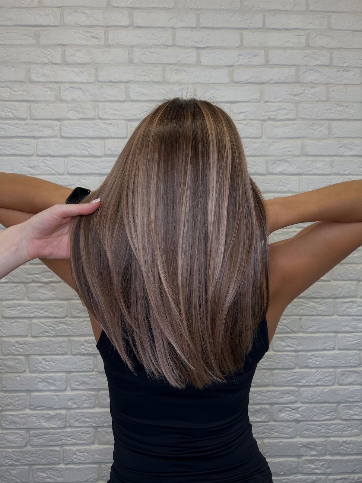Long brown hair blends into lighter blonde and brown tones against a white brick wall