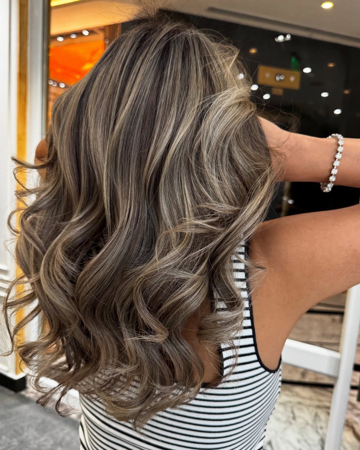 Wavy brown hair with cool ash-blonde highlights shown from behind in a salon.