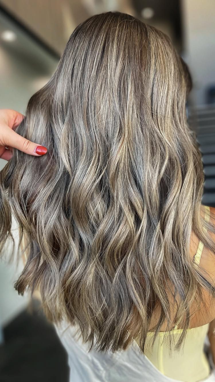 Long wavy brown hair with blonde lowlights, held aside in a salon
