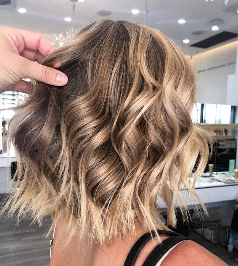 Wavy brown hair with blended golden blonde balayage highlights in a salon