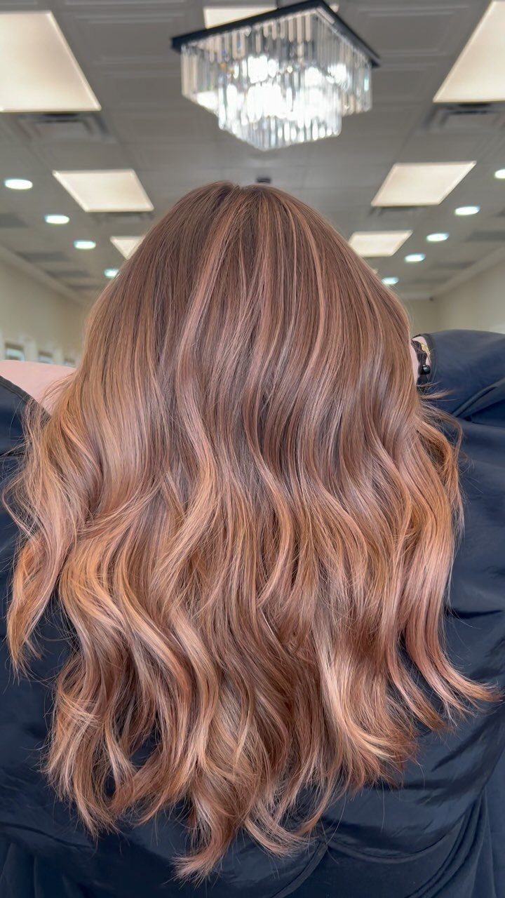 Wavy brown hair with warm strawberry-blonde balayage highlights in a salon
