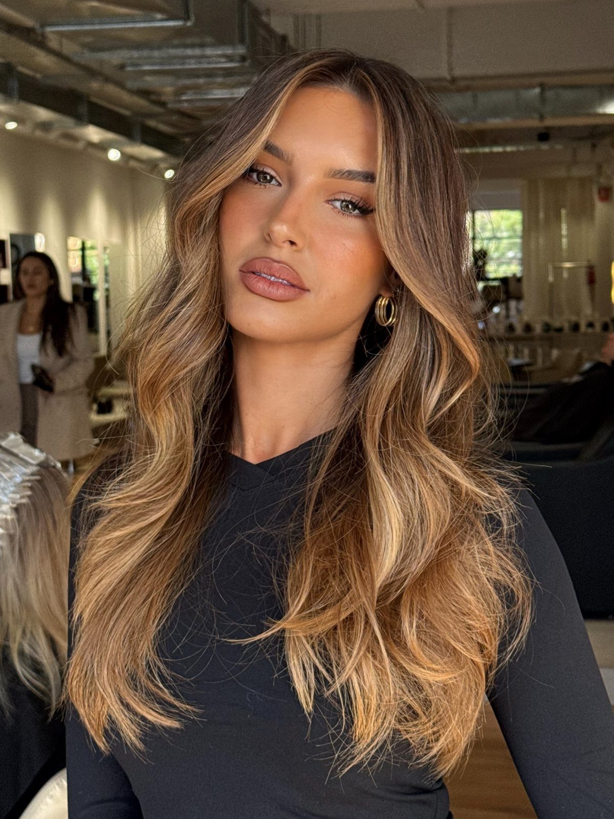 Woman with long wavy brown hair featuring blended caramel and blonde shades
