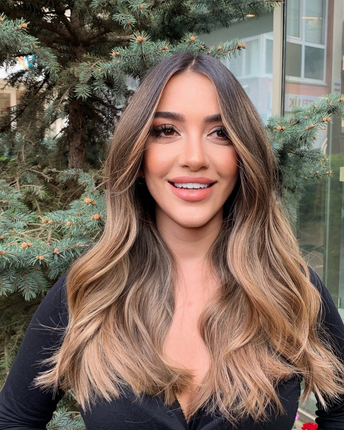 Woman showing dark brown roots fading into warm caramel blonde wavy ends