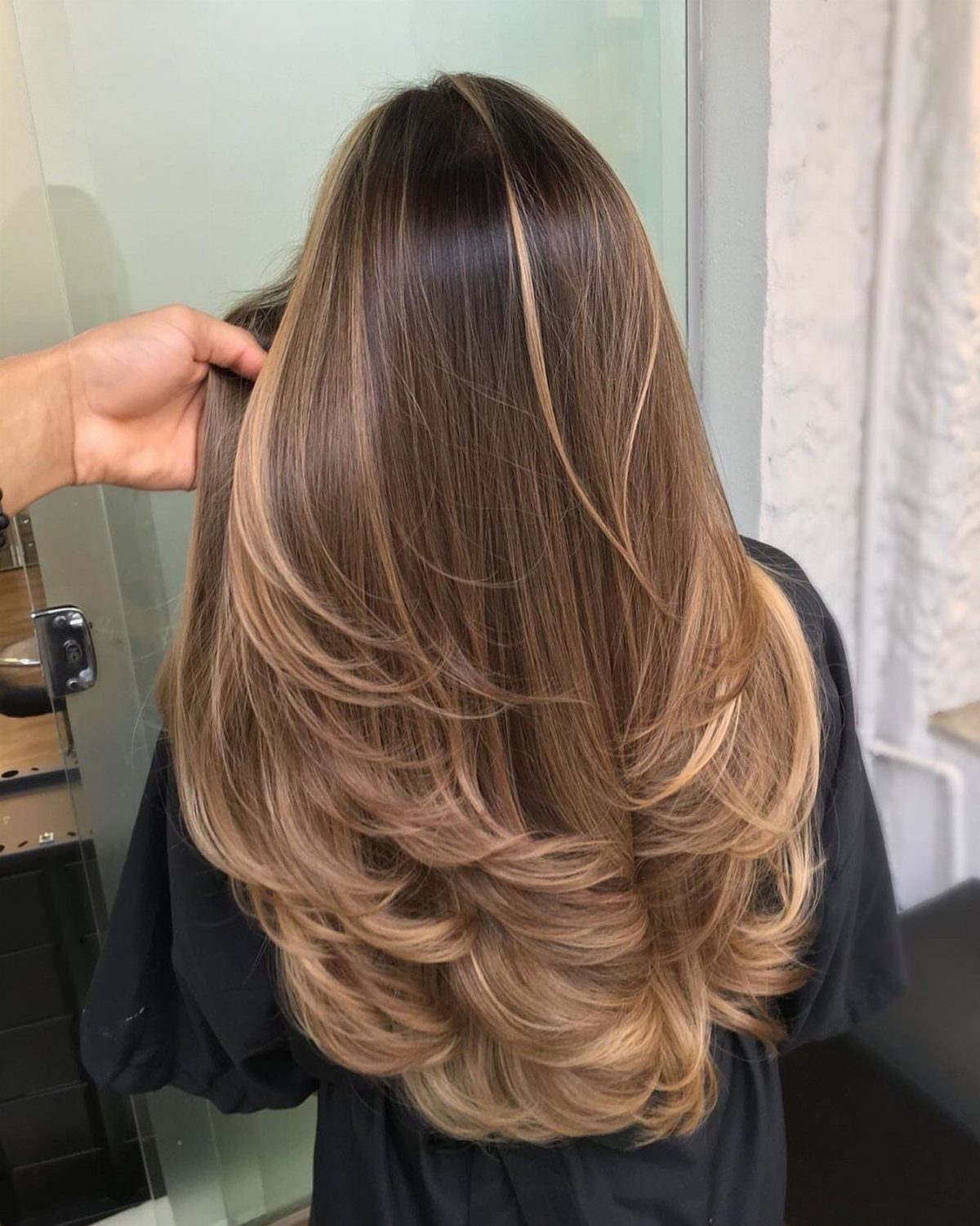Layered hair fades from dark roots into cool, light caramel-blonde curls