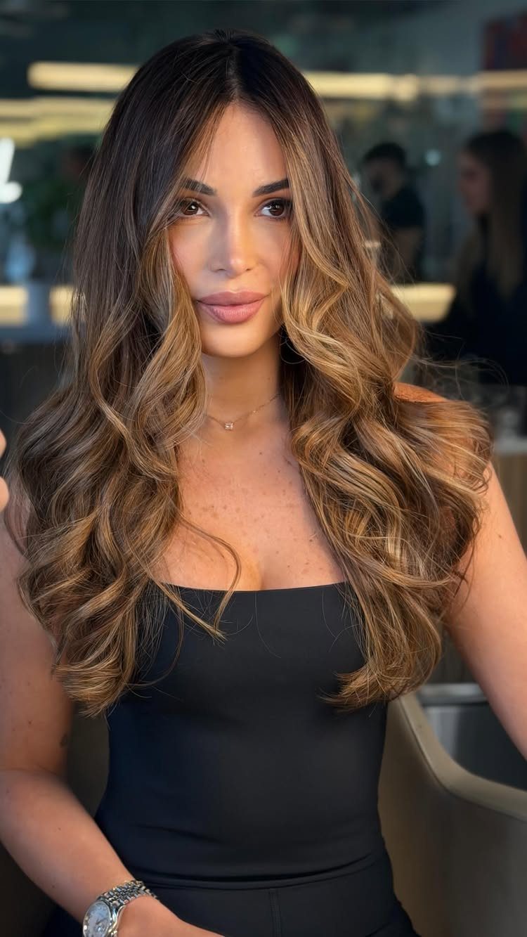 Woman showing long brunette balayage with warm caramel waves