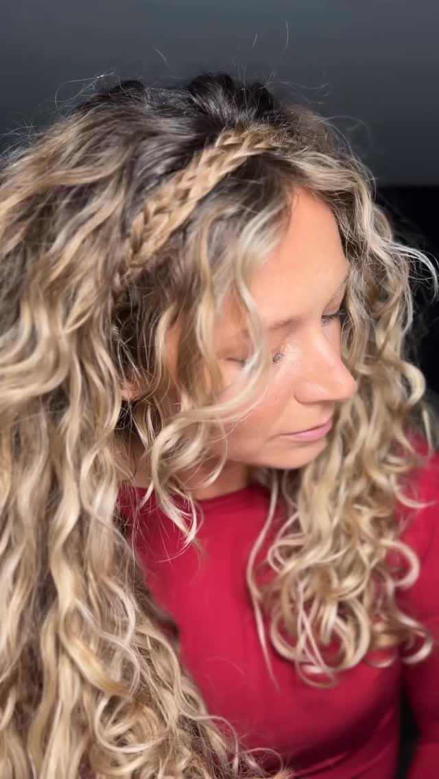 Woman showing long blonde curls with a small side braid and a red top