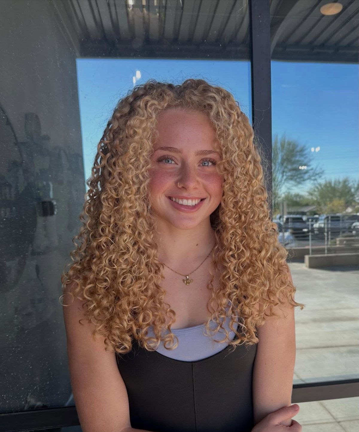Young woman with long blonde curls smiling in front of a glass wall
