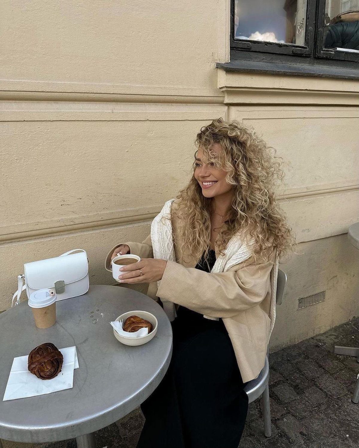 Blonde woman with long curly hair smiling at an outdoor café table