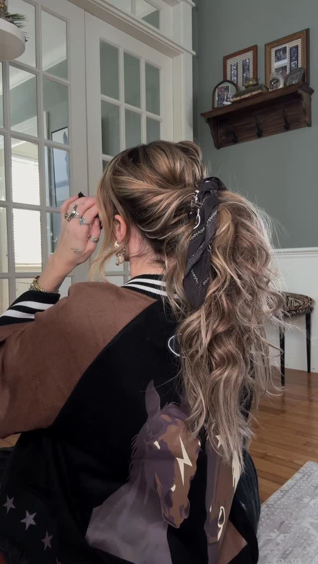 Long blonde curls gathered into a ponytail with a dark scarf