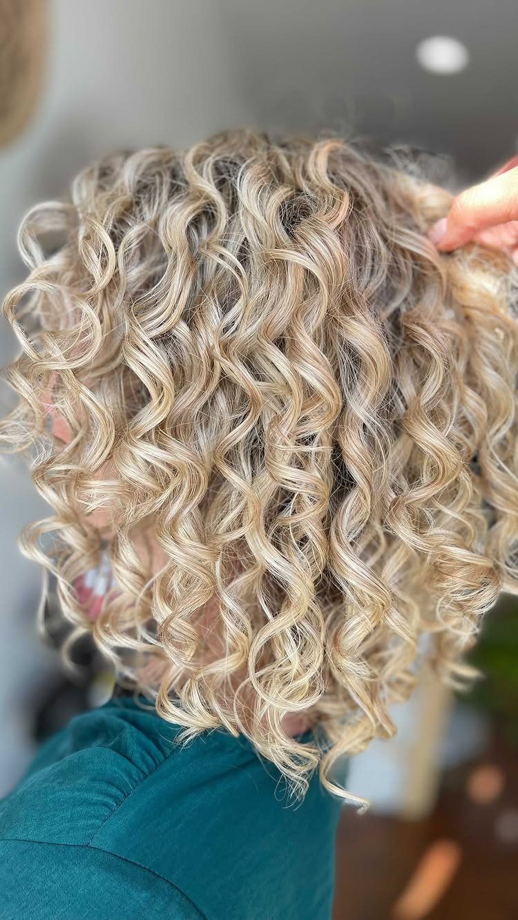 Blonde curly hairstyle with defined shoulder-length ringlets and a hand touching the hair