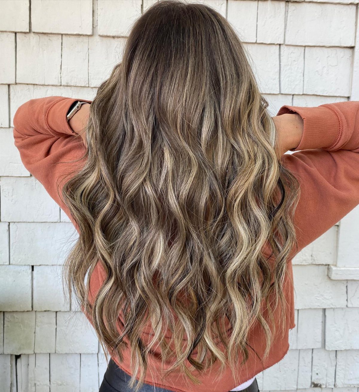 Wavy brown hair with blonde and caramel highlights falls over a coral sweater