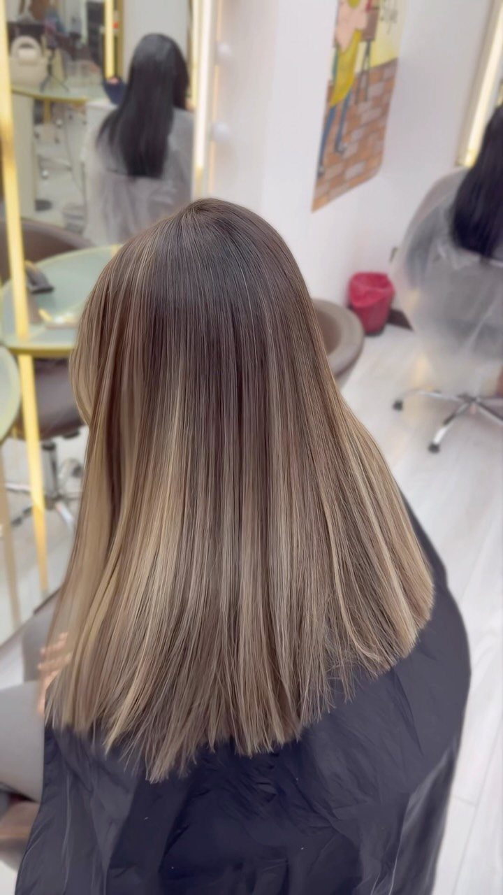 Straight ash blonde hair with darker roots shown from behind in a salon