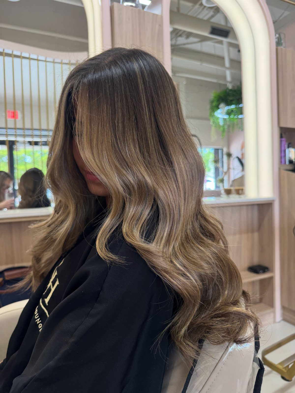 Long chestnut-brown hair with warm blonde highlights styled in loose salon waves