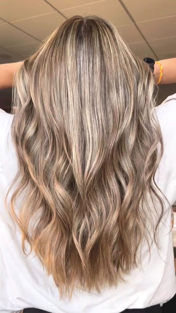 Long wavy blonde hair with dark roots and muted brown-toned strands