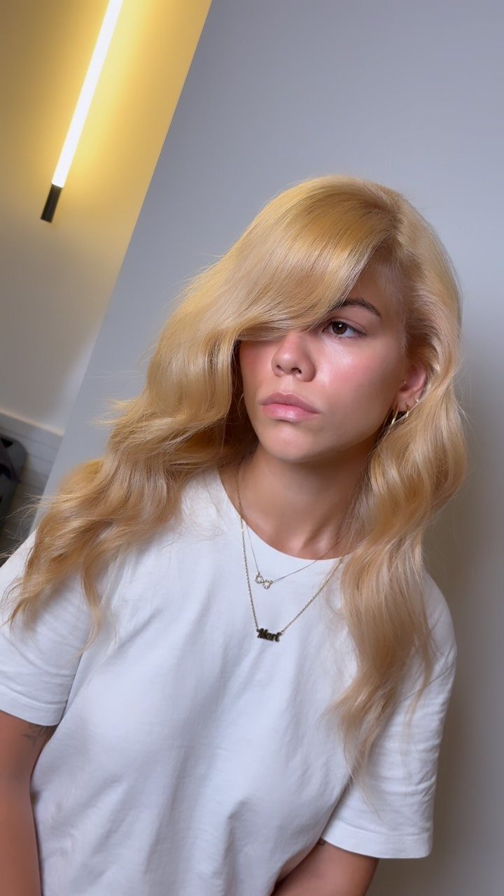 Golden platinum blonde hair with warm tones, layered lengths, and side-swept bangs