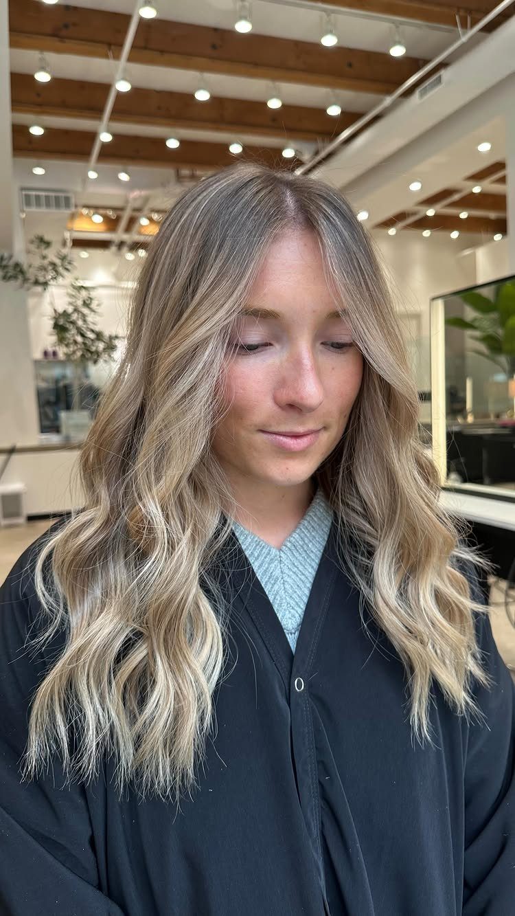 Long wavy sandy-beige blonde hair with darker roots in a salon