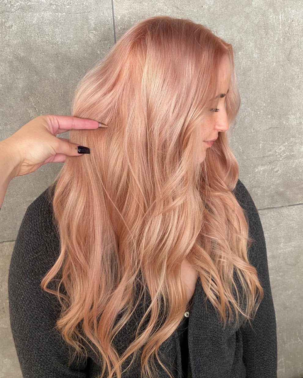 Woman with long, wavy strawberry blonde hair against a gray wall
