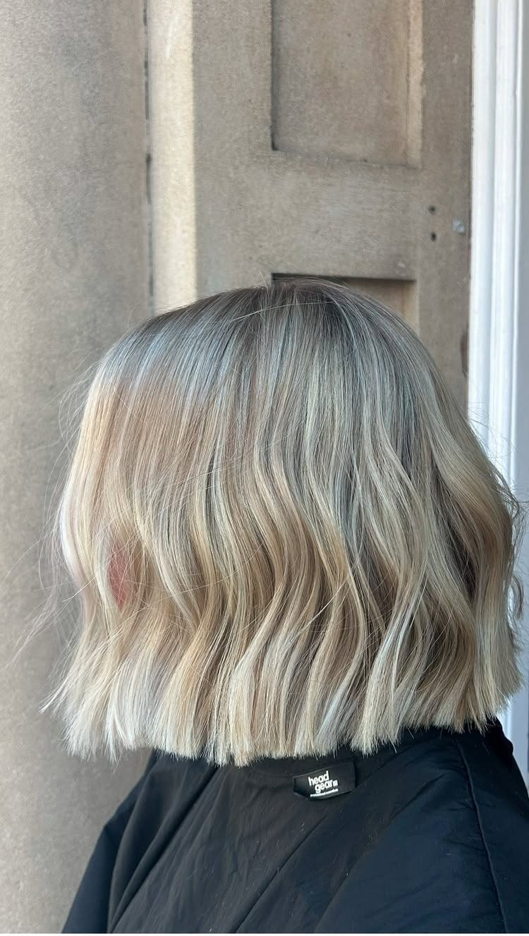 Wavy shoulder-length sandy blonde hair with pale sunny highlights in a salon cape